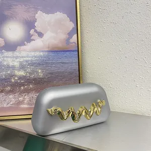 Detail view of silver matte box clutch with shiny gold wave metal decor for evening party dress.