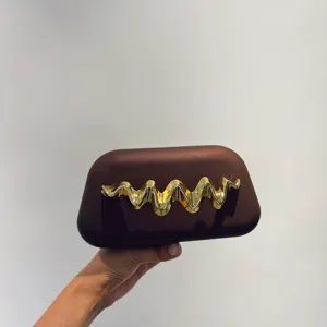 Close-up detail of a brown frosted hard-case clutch bag with a stunning gold wave metal clasp.