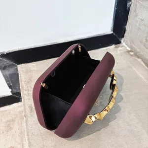 Close-up detail of burgundy matte box clutch bag featuring unique gold wave handle and clasp.