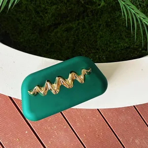Green matte clutch bag detail featuring a golden wave metal accent on the textured surface.
