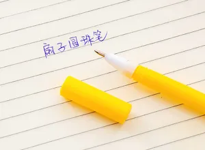 Detailed close-up shot of a cute yellow fan ballpoint pen resting on lined notebook paper.