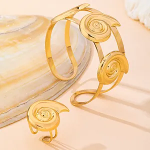 Detalle de primer plano de pulsera y anillo con diseño de espiral de caracola dorada.