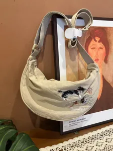 Detailed view of beige nylon dumpling crossbody bag featuring cute cat embroidery design.