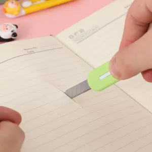 Primer plano de mini cúter portátil cortando papel en cuaderno, vista detallada.