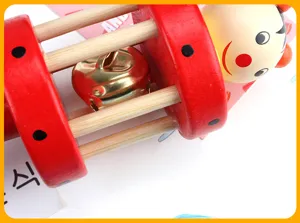 Wooden baby rattle toy with internal golden bell and cute cartoon puppet head detail shot.