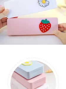 Close-up detail of cute cartoon pencil box with 3D strawberry and daisy charms for students.
