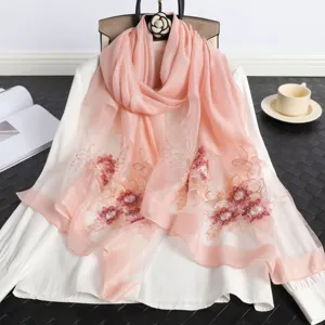 Primer plano de elegante bufanda de seda rosa con bordado floral y detalles de abalorios.