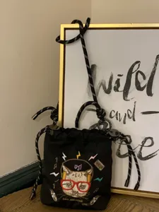 Detailed view of black drawstring canvas shoulder bag featuring cute embroidered cat.
