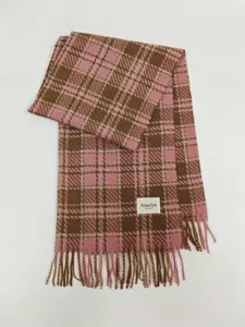 Close-up detail of cozy pink and brown plaid scarf with soft fringe and brand label.