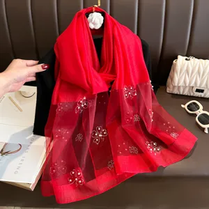 Detailed close-up of vibrant red long scarf featuring elegant pearl and rhinestone art.