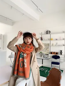 Nahaufnahme des modischen Schals aus Kaschmirimitat mit Buchstabenmuster in Orange.
