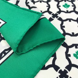 Primo piano dettagliato di foulard in seta con bordi verdi e motivo geometrico elegante.