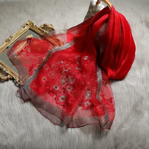 Red silk wool embroidered scarf detail, floral shawl with silver border on fluffy grey rug.