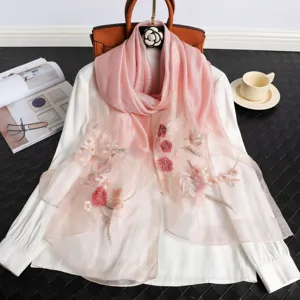 Dettaglio foulard di seta rosa sfumato con squisita ricamo floreale su camicetta bianca.