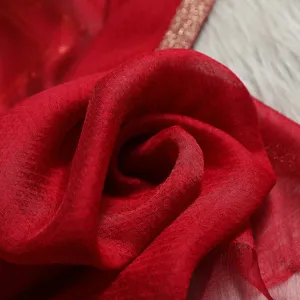 Close-up detail of red silk scarf fabric, showing elegant texture and golden border design.
