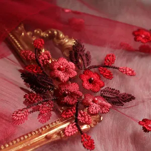 Close-up detail of red silk embroidered scarf with pearls, featuring exquisite floral lace texture.