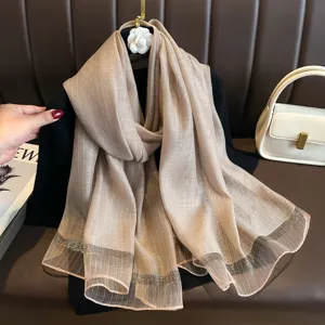 Detail view of elegant beige striped imitation silk scarf with sparkly hem and texture.