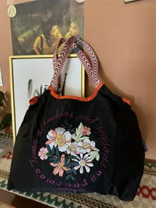 Grande borsa a tracolla con ampia spallina intrecciata e delicato ricamo floreale elegante.