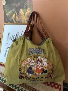 Vista dettagliata della borsa a tracolla verde oliva con ricamo di coniglio e ampia tracolla tessuta.