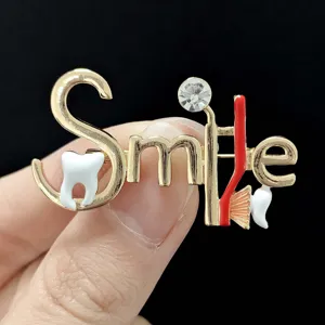 Detailed view of creative dental theme gold metal letter brooch pin with tooth and toothbrush.