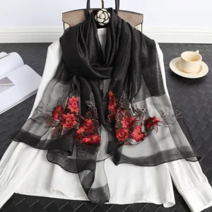 Primer plano detallado de un pañuelo negro transparente con bordado floral rojo y cuentas.