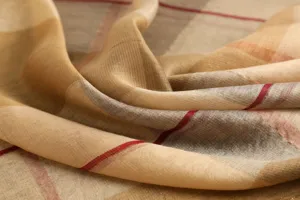 Close-up detail of luxurious plaid scarf fabric, soft draped texture, elegant beige and red check pattern.
