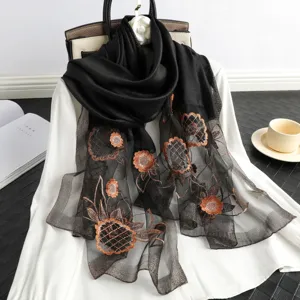 Detail view of black sheer floral embroidered scarf draped gracefully over white blouse and props.