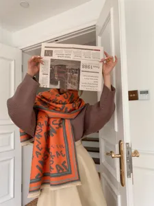 Weicher orangefarbener Schal in Kaschmir-Optik mit modernen grauen Buchstaben.
