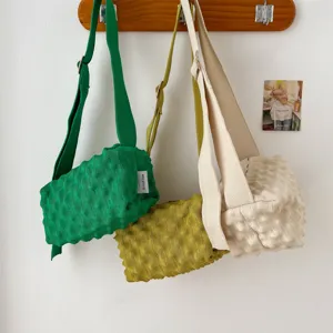 Close-up detail of three colorful knitted bubble crossbody bags hanging on wooden hook.