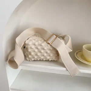 Beige knitted crossbody bag with popcorn texture, wide strap and metal buckle detail.