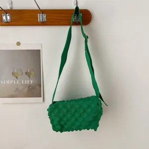 Green knitted bubble texture crossbody bag detail view hanging on clean white wall hook.