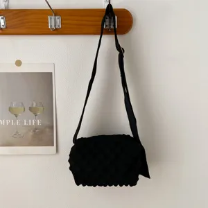 Detail view of a black knitted bubble shoulder bag hanging on a wooden wall hook.