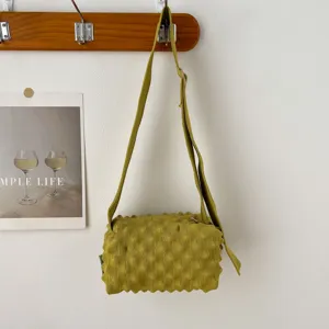 Detail shot of green knitted puckered crossbody bag hanging on wall hook, textured fabric.