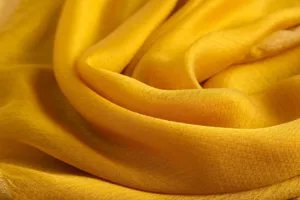 Detailed close-up shot of luxurious yellow silk wool scarf and elegant draped shawl texture.