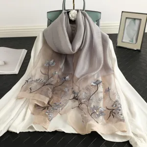 Detail view of grey and beige silk wool scarf featuring delicate lotus embroidery and soft drape.