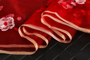 Detail shot of red silk scarf with delicate floral embroidery and gold trim edge.