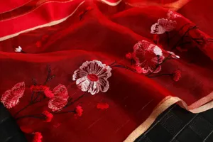 Detailed shot of red silk wool embroidered scarf with delicate floral patterns and gold trim.