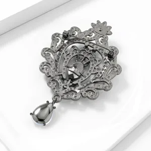 Gedetailleerd overzicht van de vintage zwarte metalen filigrain broche met hangende druppel glas.