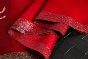 Red silk wool scarf detail closeup, elegant metallic embroidered border, soft texture fabric.