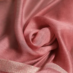 Vista detallada de una bufanda rosa de seda y lana con motivo de espiga y bordes metálicos.