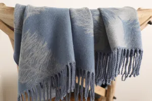 Detailed close-up of a soft blue cashmere scarf with delicate feather patterns and tassels.