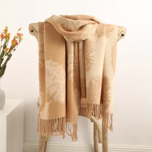 Detailed view of beige cashmere scarf featuring feather pattern and elegant tassels on wooden chair.