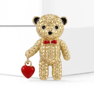 Detailed view of gold-tone textured teddy bear brooch with red heart charm and bow.