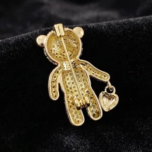 Close-up detail of a gold-tone alloy teddy bear brooch with pin back and heart pendant.