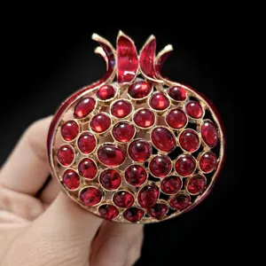 Exquisita broche en forma de granada con piedras rojas vibrantes y montura dorada elegante.