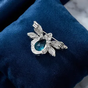 Close-up detail of silver tone alloy bee brooch featuring a blue crystal stone back pin.