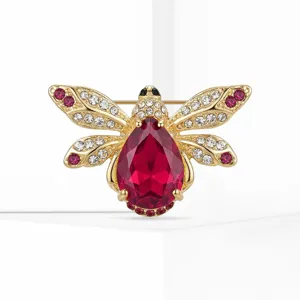 Detailed close-up of a gold-tone rhinestone bee brooch featuring a striking red crystal gemstone.
