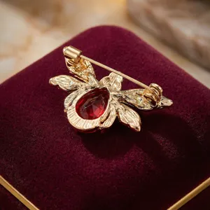 Close-up detail of a gold-tone bee brooch featuring a sparkling red gemstone on velvet.