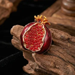 Exquisito detalle de broche de granada, esmalte rojo y metal dorado con cuentas rojas vibrantes.