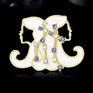 Primo piano spilla segno zodiacale Gemelli, metallo dorato smalto bianco e dettagli in cristallo.